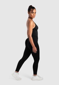 Czarny sportowy bodysuit z cienkimi ramiączkami, zestawiony z czarnymi legginsami i białymi sneakersami. Gładka tekstura, dopasowany krój bez wzorów.