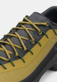 Primer plano de una bota de senderismo amarilla y gris con cordones verdes y amarillos y detalles de malla transpirable en el costado.