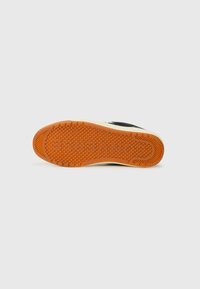 Black sneaker with a textured rubber sole featuring a honeycomb pattern and an orange accent. Sturdy construction with reinforced areas.