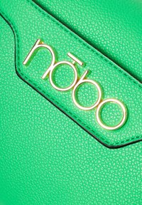 Borsa sintetica verde con superficie testurizzata, caratterizzata da un logo "nōbo" in tonalità dorata e cuciture scure lungo i bordi.