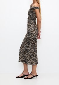 Robe à imprimé léopard en tissu doux, présentant un design épaules dénudées et un détail froncé le long du corsage, avec une silhouette fluide.