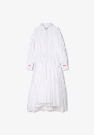 Robe en coton blanche à manches longues, à boutons sur le devant et jupe froncée. Des accents de texte rouges notables sur les poignets des manches indiquent "ZADIG" et "VOLTAIRE."