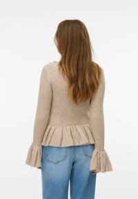 Maglione beige a coste con maniche svasate e orlo peplum, realizzato in un morbido materiale a maglia. Abbinato a jeans a vita alta blu chiaro.