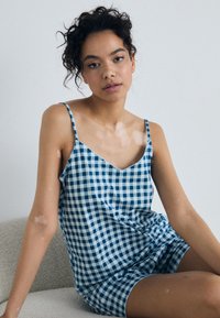 Blue and white gingham camisole with thin straps and a V-neckline, featuring a relaxed fit and a scalloped hem. Soft fabric texture.