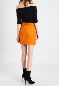 Haut noir à épaules dénudées et mini-jupe en velours côtelé orange vif avec deux poches arrière. Porté avec des bottines noires.