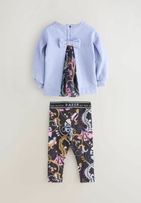 Top a maniche lunghe lilla con fiocco sulla schiena e inserto a motivo floreale, abbinato a leggings neri con stampa floreale e vita con logo.