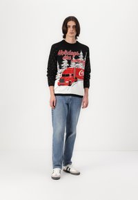 Pletený sveter s čiernym telom, bielymi snehovými vločkami, dizajnom červeného auta a textom "Prichádzajú sviatky". Kombinovaný s modrými džínmi.