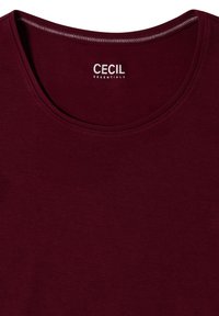 T-shirt rouge foncé à col rond avec coutures visibles et étiquette de marque blanche "CECIL ESSENTIALS" à l'intérieur de l'encolure.
