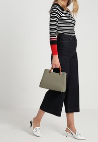 Olijfgroene handtas met houten handvatten, gecombineerd met een gestreepte zwart-wit top, donkere wijde jeans en witte slingbacks.