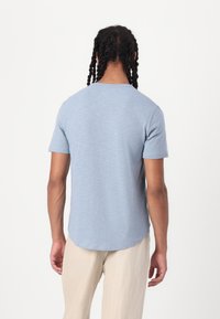 Camiseta de manga corta azul claro con dobladillo redondeado y textura suave, que presenta un escote redondo y un corte relajado.