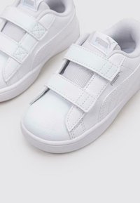 Białe buty sportowe z gładką skórzaną cholewką, akcentami z siateczki i dwoma paskami na rzepy. Dyskretny detal z logo z boku.