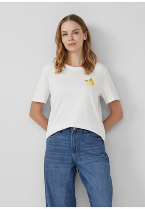 White cotton t-shirt with short sleeves, featuring a small yellow lemon graphic on the left chest, paired with blue denim jeans.