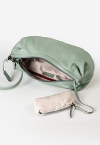 Lichtgroene leren polsbandtas met een open rits die de gestreepte stofinterieur toont, naast een opgevouwen crèmekleurige gestreepte pouch met rits.