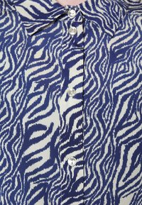Tissu imprimé zèbre bleu et blanc avec quatre boutons blancs visibles et un col sur une chemise ou un chemisier.