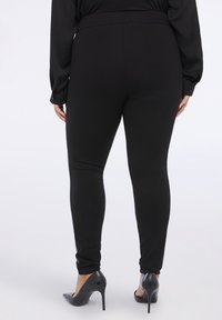 Svarta stretchiga leggings med hög midja, med en mjuk yta och figurnära design, kombinerade med glansiga svarta stilettklackar.