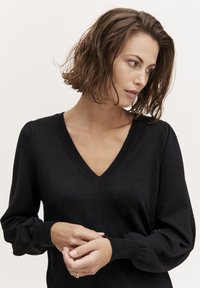 Maglione nero lavorato a maglia con scollo a V e maniche a sbuffo. Texture morbida, corpo aderente e polsini a coste. Design semplice e classico.
