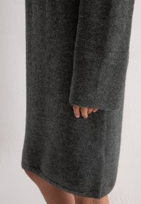 Robe en laine grise à manches longues. Tissu doux et texturé, longueur genoux, avec une coupe droite et un ourlet subtil.