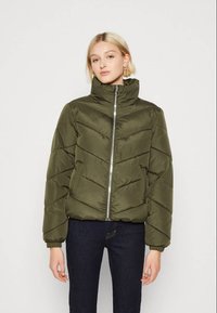 Oliwkowa kurtka puchowa z wysokim kołnierzem, zamek błyskawiczny na przodzie oraz wzór w chevron. Posiada elastyczne mankiety i dwie boczne kieszenie.