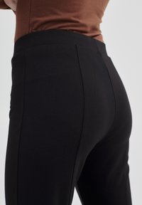 Pantalons noirs ajustés avec une texture lisse et une taille élastique. Présente un design de dos sans couture et un minimum de coutures pour une apparence épurée.