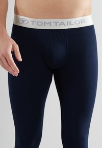 Leggings azul oscuro hechos de una tela elástica. Presenta una cinturilla elástica de color claro con el logo "TOM TAILOR". Textura suave, diseño ajustado.