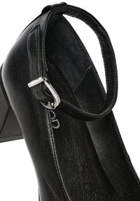 Zapato de tacón alto negro con puntera redonda, textura de cuero suave, correa al tobillo y detalle de hebilla de metal plateado.