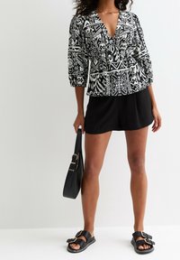 Blusa a righe in bianco e nero con scollatura a V profonda e maniche a palloncino, abbinata a pantaloni corti neri e sandali piatta. Tiene una borsa nera.