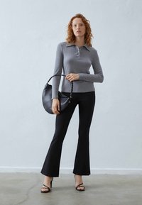Grijze geribbelde lange mouw top met een kraag, gecombineerd met zwarte flair broeken en een zwarte leren schoudertas. Gestrikte hakken maken de look compleet.