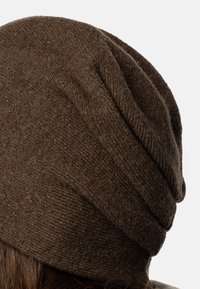 Brun strik beanie lavet af blødt uld. Har et slouchy design med en tekstureret finish og subtile folder øverst.