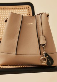 Sac seau en cuir beige avec des accents noirs, logo doré et détail de porte-clés. Texture lisse et forme arrondie avec une fermeture zippée.