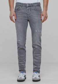 Vihreät farkut haalistuneessa harmaassa sävyssä, slim fit -mallilla, jossa on kevyitä kulutuksia reisissä ja viisi taskua. Parina valkoiset ja harmaat lenkkarit.