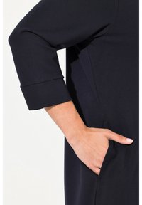 Navyblaues Kleid mit 3/4-Ärmeln, ausgestattet mit einer Seitentasche und einer glatten Textur. Der Ärmel hat ein gefaltetes Aufschlagdetail.