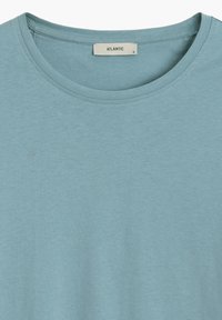 Jasnoniebieska koszulka z okrągłym dekoltem, wykonana z miękkiego materiału. Posiada krótkie rękawy oraz metkę z napisem "ATLANTIC" i rozmiarem "S". Minimalna faktura.
