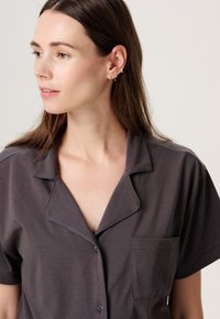 Korte mouwen, geklede overhemd in donkergrijze stof. Heeft een borstzak en subtiele stikseldetails. Gladde textuur, losse pasvorm.