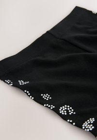 Črno tkano blago na vrhu z okraski iz majhnih, svetlikajočih se srebrnih zatičev v različnih vzorcih ob robu. Mehka tekstura z gladkim zaključkom.