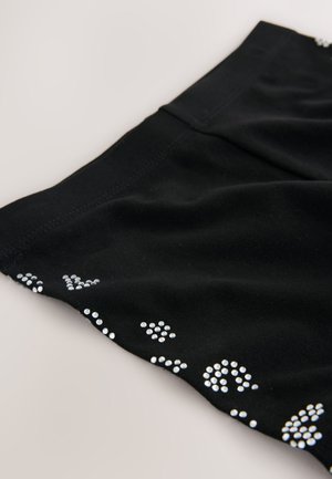 Fekete szövet felsőrész, melyen kis, fényes ezüst szegecsek díszítik a szegélyt változatos mintákban. Puha anyag, sima felülettel.