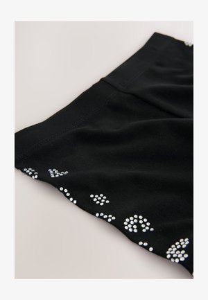 Schwarzes Stoffoberteil mit Verzierungen aus kleinen, glänzenden silbernen Nieten in verschiedenen Mustern entlang des Saums. Weiche Textur mit glattem Finish.