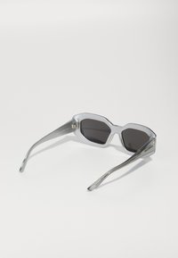 Lunettes de soleil hexagonales argentées avec des verres foncés, une texture mate et des branches en métal arborant des détails de logo sur les côtés.