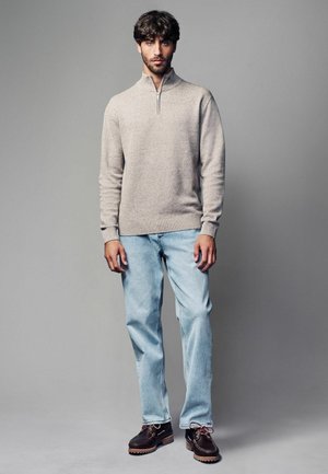 Beige zip-up knit sweater, light blue straight-leg jeans, and brown lace-up boots with rubber soles. Simple design and textured fabric.