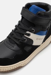 High-top sneakers featuring a black leather upper with suede accents, blue and white stripes, and a cream-colored rubber sole. Includes lace and strap closure.