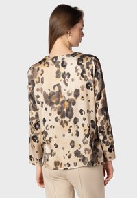 Blusa in satin con stampa leopardata, caratterizzata da un colletto rotondo, maniche lunghe e una vestibilità comoda. Il colore di base è beige con macchie nere e marroni.
