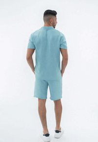 Polo bleu clair à manches courtes et short assorti en tissu texturé, avec un col classique et une coupe décontractée. Baskets blanches.