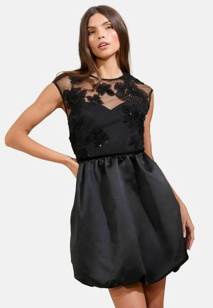 Black dress featuring a sheer mesh bodice adorned with floral embroidery. The skirt is gathered, creating a voluminous silhouette.