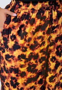 Oranga och svarta mönstrade byxor med vida ben och elastisk midja, tillverkade av ett flytande, lätt tyg med en djärv, abstrakt design.