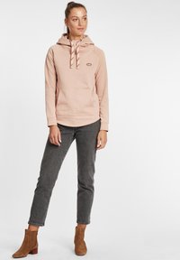 Hoodie rosa chiaro con motivo testurizzato, cappuccio regolabile con cordino e tasca frontale. Abbinato a jeans grigi e stivaletti marroni.