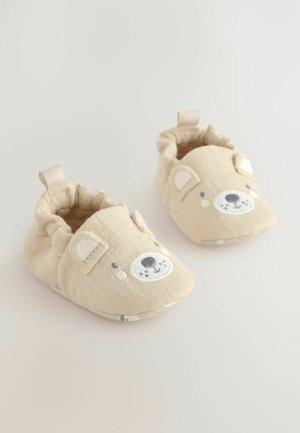 Pantofole beige per bambini con un design a faccia di orso; caratterizzate da tessuto morbido, forma arrotondata e una linguetta posteriore per un facile indossamento.