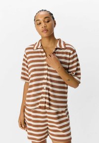 Gestreept bruin en crèmekleurig lichtgewicht gebreid shirt met korte mouwen, een kraag en knopen, gecombineerd met bijpassende shorts.