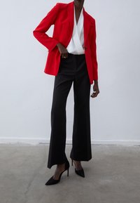 Veste rouge à épaulettes structurées, haut blanc à nouer et pantalon noir taille haute. Fini avec des talons aiguilles noirs pointus.