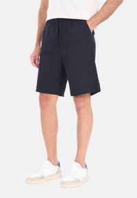Shorts in cotone blu navy con vita elastica, tasche frontali e taglio dritto, abbinati a sneaker bianche con accenti grigi e blu.