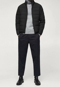 Veste rembourrée noire, pull à col roulé gris, pantalon à rayures fines, et bottines noires. Caractérisée par une fermeture éclair à l'avant et un col montant.