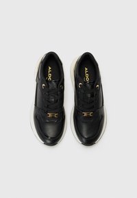 Baskets en cuir noir avec une texture lisse, accents dorés, design à lacets, semelles rembourrées et une intercalaire blanche contrastante.